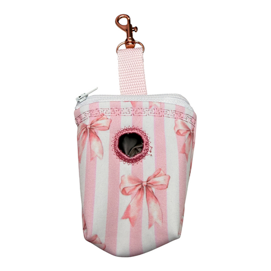 Kotbeutelspender „Wrapped in Blush“ von Doggies Couture in zartem Rosa mit romantischem Schleifenmuster. Handgefertigter Hundekotbeutelspender mit großer Öffnung zum einfachen Entnehmen der Sackerl, großem Fach für zwei Rollen und praktischem Karabiner zur Befestigung an Leine, Tasche oder Gürtel. Stilvolles Hundezubehör passend zum Matching-Look für Hund und Mensch.