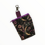 Papillon de Lune Leckerlibeutel für Hunde von Doggies Couture mit elegantem Schmetterlings-, Blumen- und Mond-Design in Rosa, Lila, Gold und Petrol auf schwarzem Hintergrund, mit Zippverschluss und praktischem Karabiner.